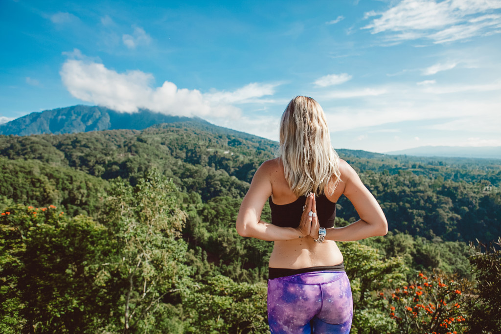 woman doing yoga while in a mountain side overlooking the greenery