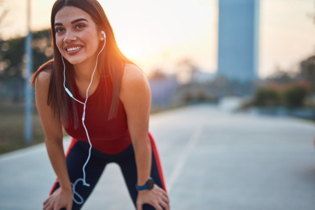 Modern young woman with cellphone making pause during jogging / exercise.
