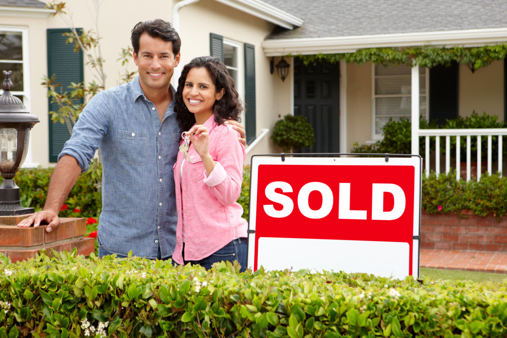 Young couple standing in front of a house with a sold sign.