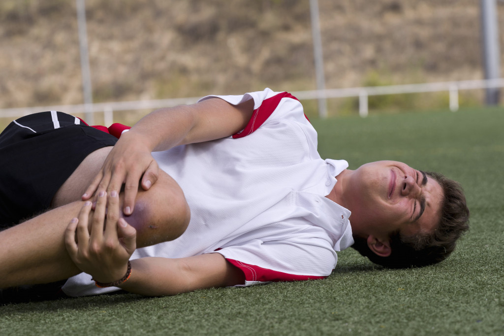 A football player is writhing in pain on the ground as a result of a physical injury.