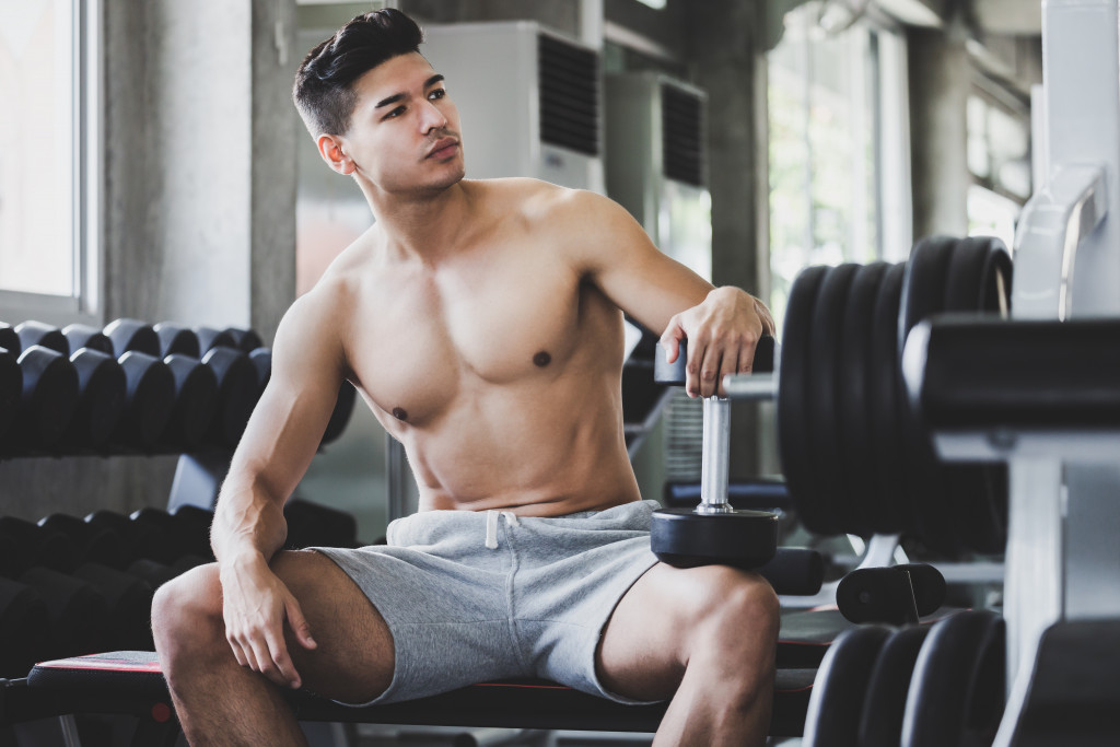 A guy sitting in a gym while holding a dumbbell
