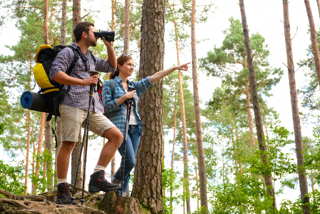 Young couple on a hiking trip with the woman pointing at one direction and the man using a pair of binoculars.